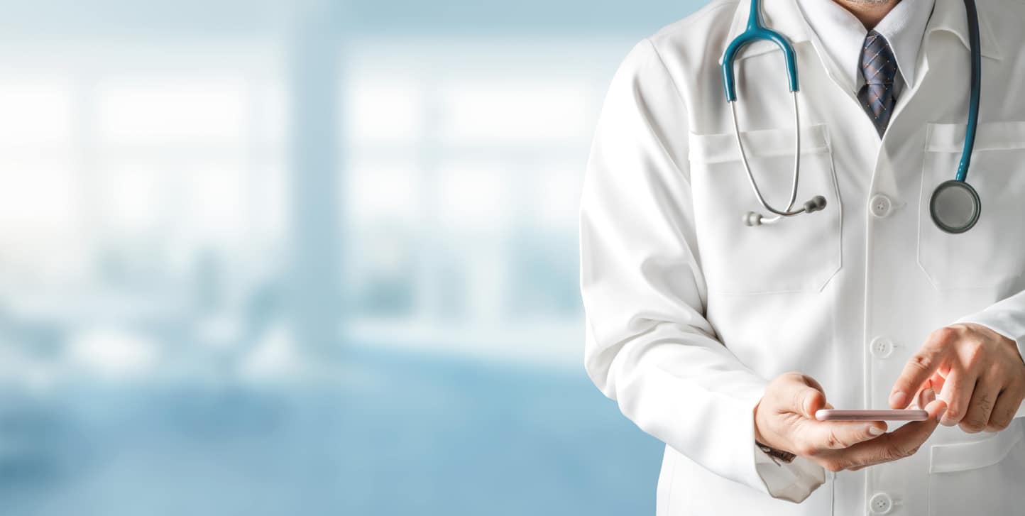 Doctor with stethoscope viewing appointments on mobile phone Infront of a blurred background.